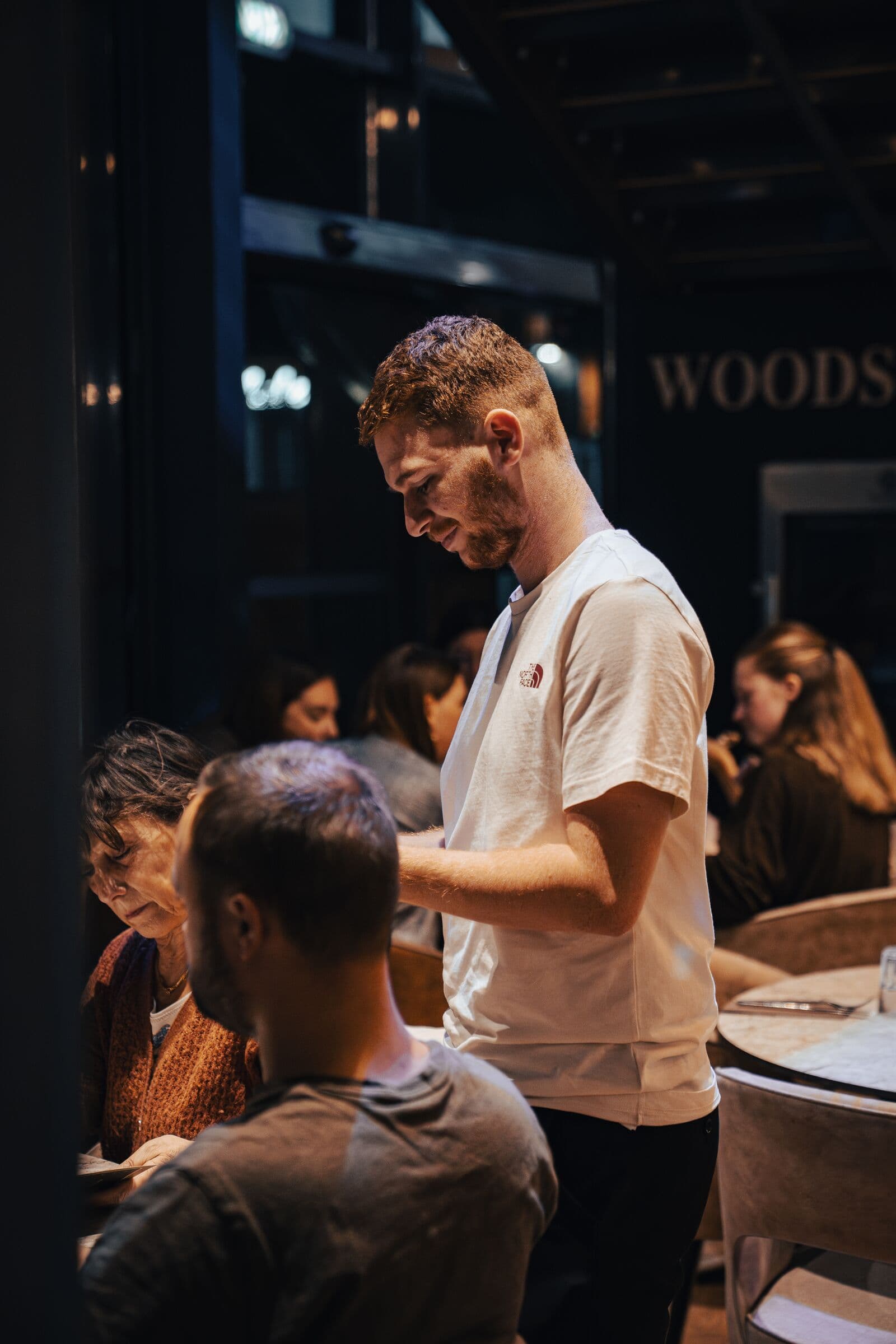 Serveur du WOODS servant une table en souriant