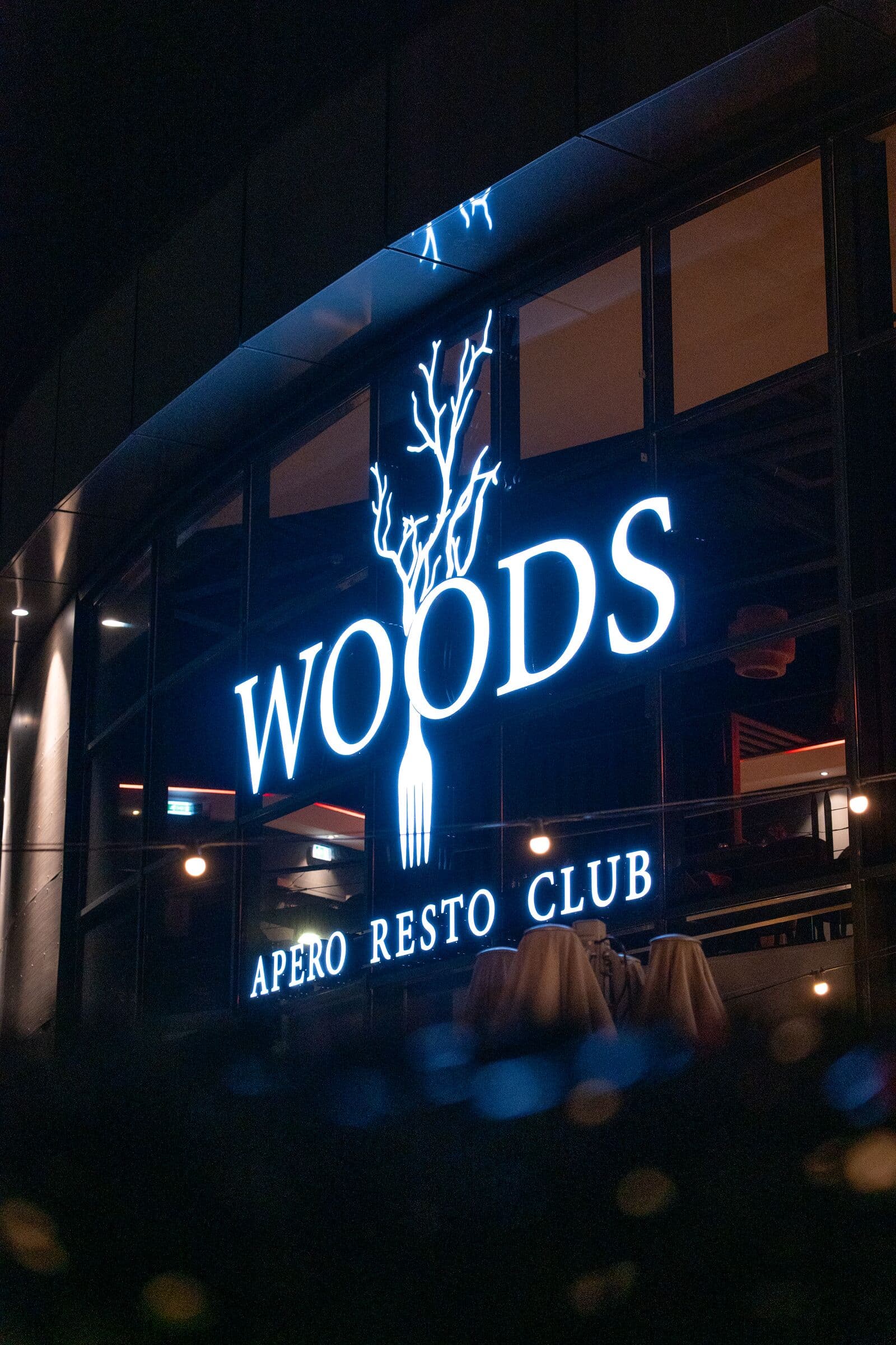 Façade du WOODS illuminée la nuit, enseigne Apéro Resto Club, restaurant à Bourgoin-Jallieu